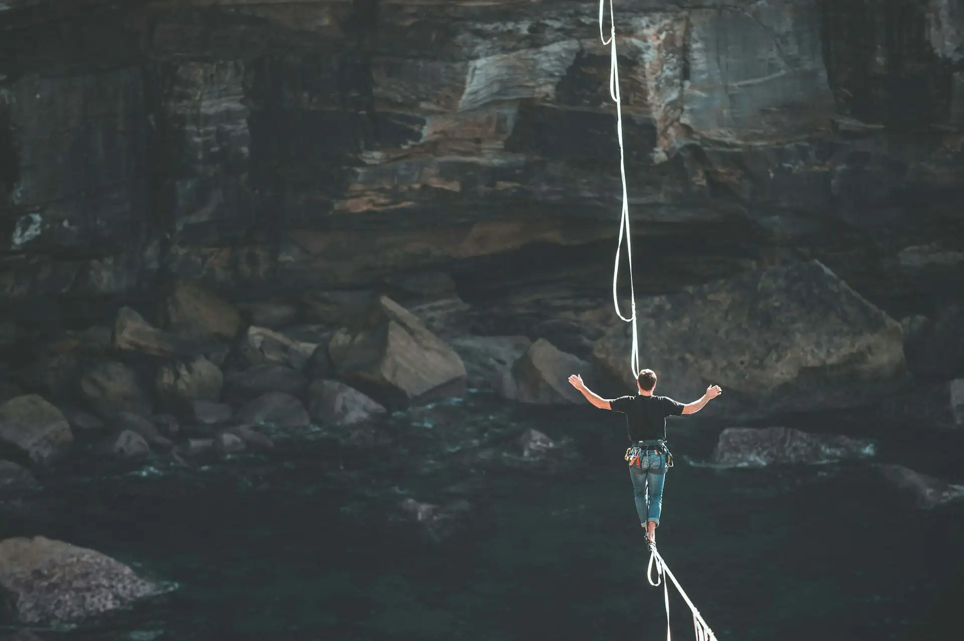 A person walking a highline strung across a dark rocky gorge